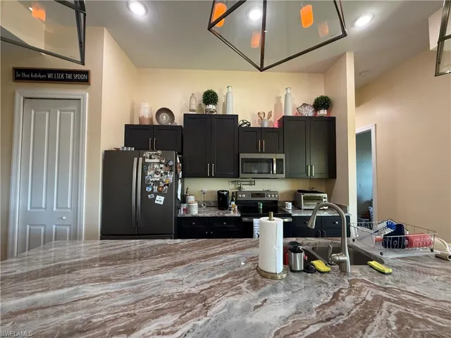 Kitchen featuring stainless steel appliances, light stone countertops, recessed lighting, and dark cabinets