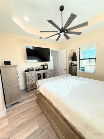 Bedroom with light wood-style flooring, ceiling fan, a tray ceiling, and recessed lighting
