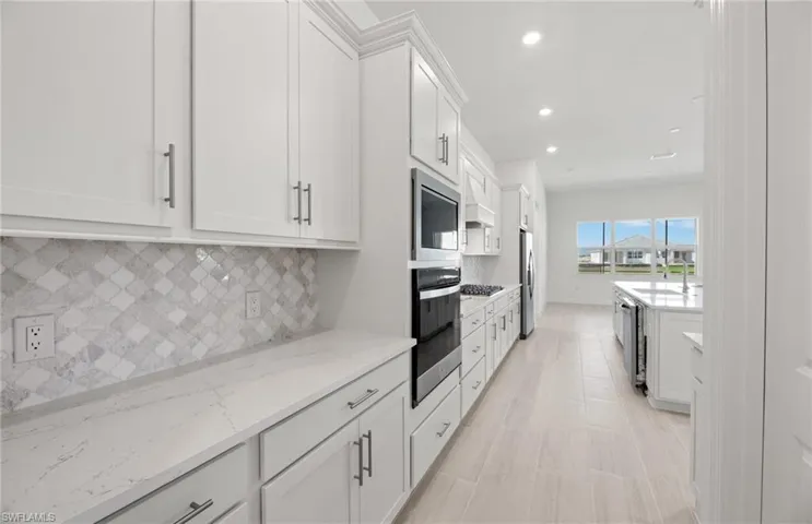 Kitchen featuring stainless steel appliances, tasteful backsplash, white cabinetry, light stone countertops, and premium range hood