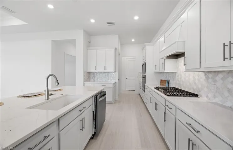 Kitchen with stainless steel appliances, tasteful backsplash, white cabinetry, light stone countertops, and sink