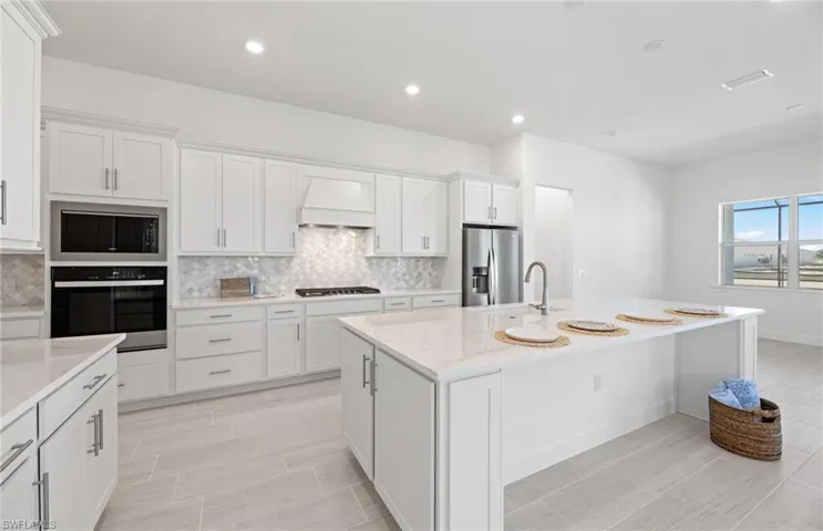 Kitchen with tasteful backsplash, an island with sink, stainless steel refrigerator with ice dispenser, custom range hood, and black oven