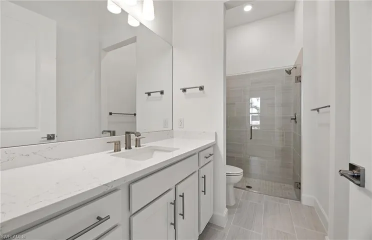 Bathroom featuring tiled shower, vanity, toilet, and tile flooring