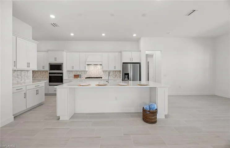 Kitchen featuring appliances with stainless steel finishes, a kitchen island with sink, light tile floors, and custom range hood
