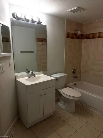Bathroom featuring bathing tub / shower combination, tile patterned floors, a textured ceiling, vanity, and a textured wall
