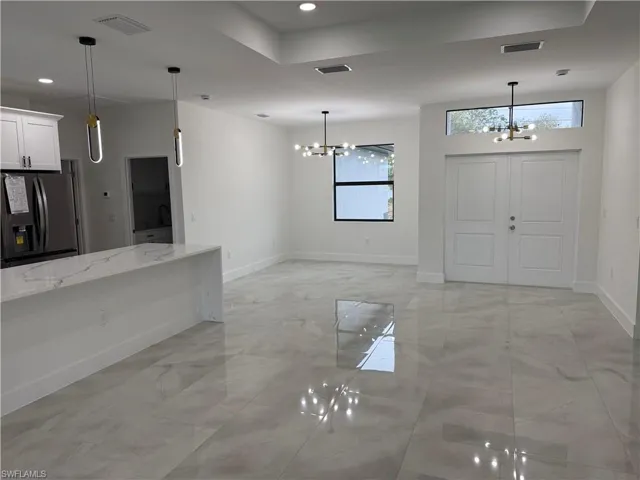 Kitchen featuring white cabinets, light stone countertops, a chandelier, and black fridge