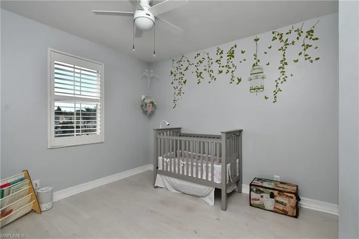 Bedroom featuring a crib, ceiling fan, and light wood-type flooring