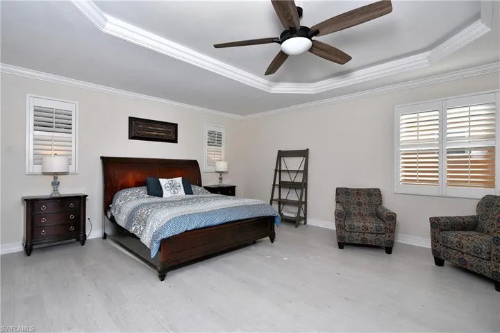 Master bedroom featuring ceiling fan, ornamental molding, a raised ceiling, and light wood-type flooring