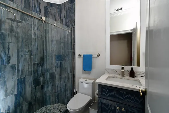 Bathroom featuring vanity, a tile shower, crown molding, and toilet