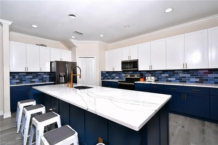 Kitchen with a breakfast bar, white cabinetry, appliances with stainless steel finishes, an island with sink, and light stone countertops