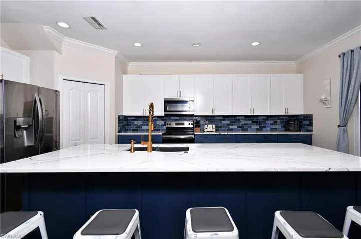 Kitchen featuring stainless steel appliances, light stone countertops, a breakfast bar area, and a large island with sink