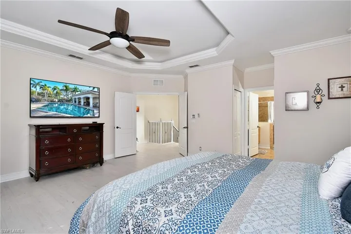 Bedroom featuring crown molding, ensuite bath, ceiling fan, a tray ceiling, and light hardwood / wood-style floors