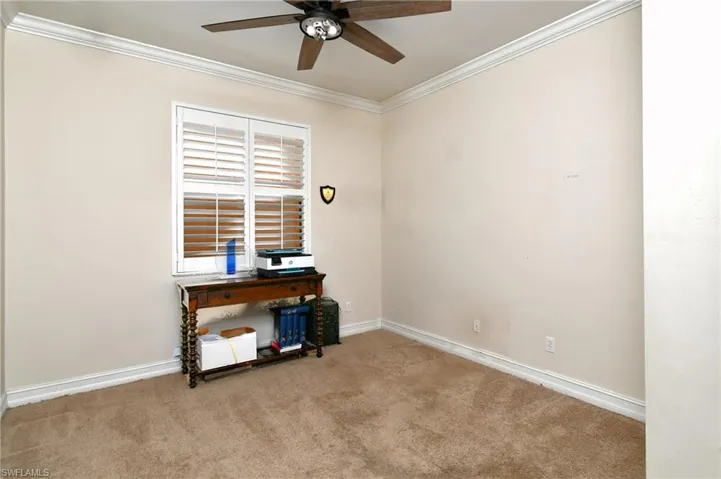 First floor bedroom with ornamental molding, light colored carpet, and ceiling fan