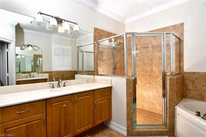 Bathroom featuring crown molding, shower with separate bathtub, and dual sinks