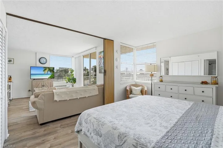 Open-concept living space with wood-finish flooring, white walls, and abundant natural light from multiple windows - Virtually Edited Image