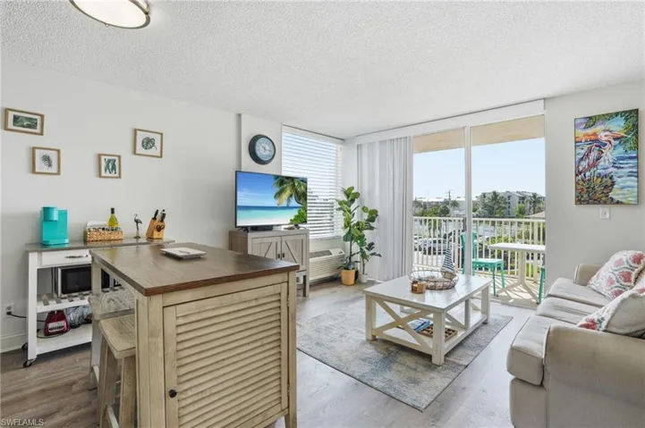 Open-concept living area with wood-finish flooring, a sliding glass door leading to a balcony, and a dedicated dining island - Virtually Edited Image