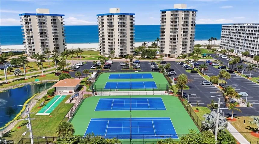Community amenities featuring multiple tennis courts, a shuffleboard court, and a reflective pond - Virtually Edited Image