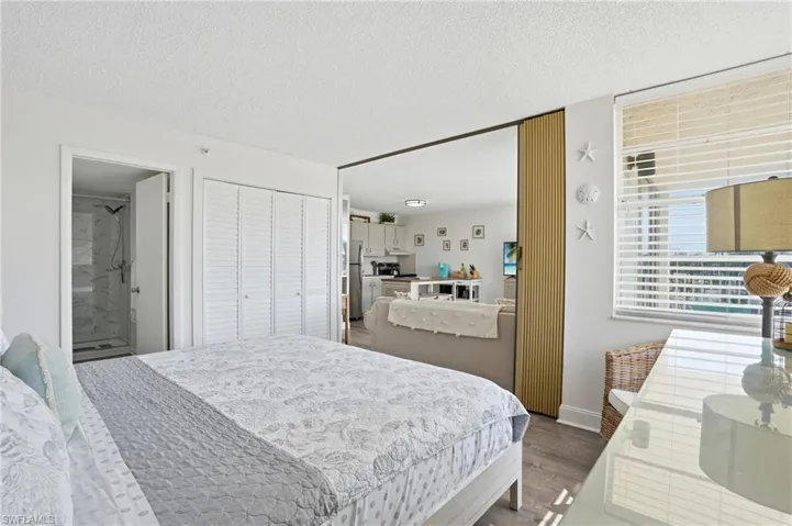 Bedroom area featuring wood-finish flooring, louvered bi-fold closet doors, and a window with horizontal blinds - Virtually Edited Image