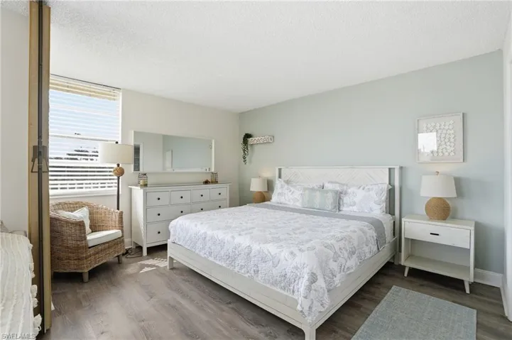 Spacious room featuring wood-finish flooring, a large window with horizontal blinds, a white paneled ceiling, and light-colored walls - Virtually Edited Image