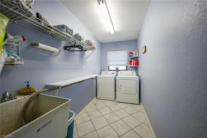 Laundry room featuring sink, light tile patterned floors, washer and dryer, and a textured ceiling