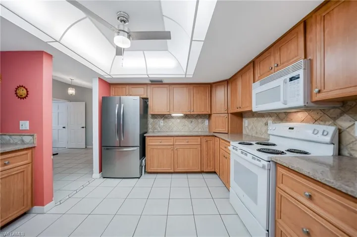 Kitchen with ceiling fan, light stone counters, backsplash, white appliances, and light tile patterned floors