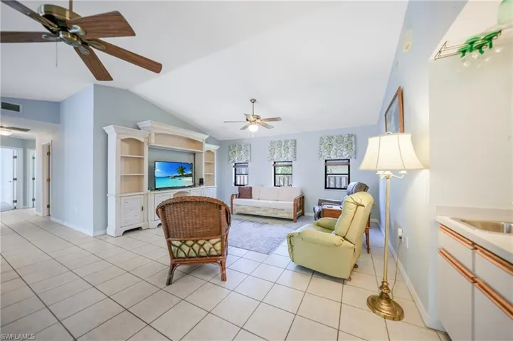 Tiled living room with ceiling fan, sink, and vaulted ceiling