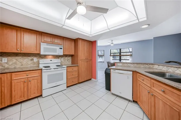 Kitchen with white appliances, sink, ceiling fan, light tile patterned floors, and tasteful backsplash