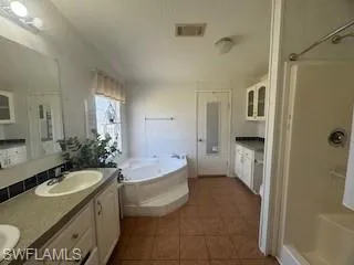 Bathroom with double vanity, a bath, a stall shower, a textured ceiling, and light tile patterned floors and walk in closet