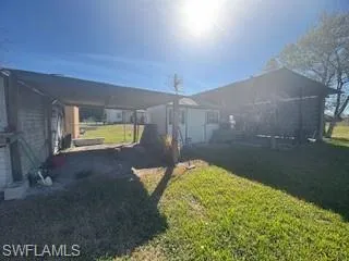 View of grassy yard with a workshop, and attached carport, and a storage shed