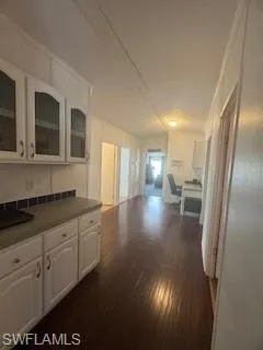 Hallway featuring white cabinetry, dark countertops, dark wood finished floors, and glass insert cabinets