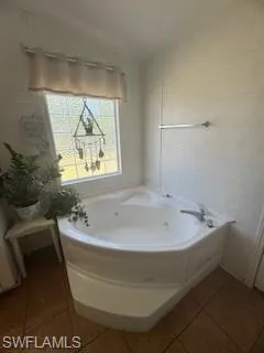 Full bathroom featuring light tile patterned flooring, a jetted tub, and vaulted ceiling