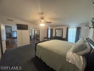 Carpeted bedroom with ensuite bath, ceiling fan, and lofted ceiling