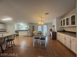 Kitchen featuring white cabinets, dark countertops, stainless steel fridge with ice dispenser, hanging lights, and plenty of natural light