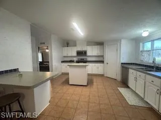 Kitchen with white cabinets, a breakfast bar area, dark countertops, and stainless steel appliances