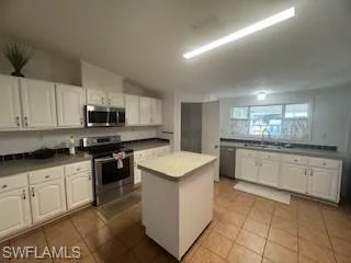 Kitchen featuring white cabinets, stainless steel appliances, a portable kitchen island, and light tile patterned floors
