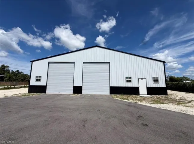 Metal building with a two-tone exterior, featuring two large roll-up doors, a pedestrian entry door, and multiple framed windows