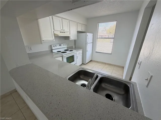 Kitchen featuring light tile patterned floors, white appliances, a textured ceiling, white cabinets, and light stone countertops