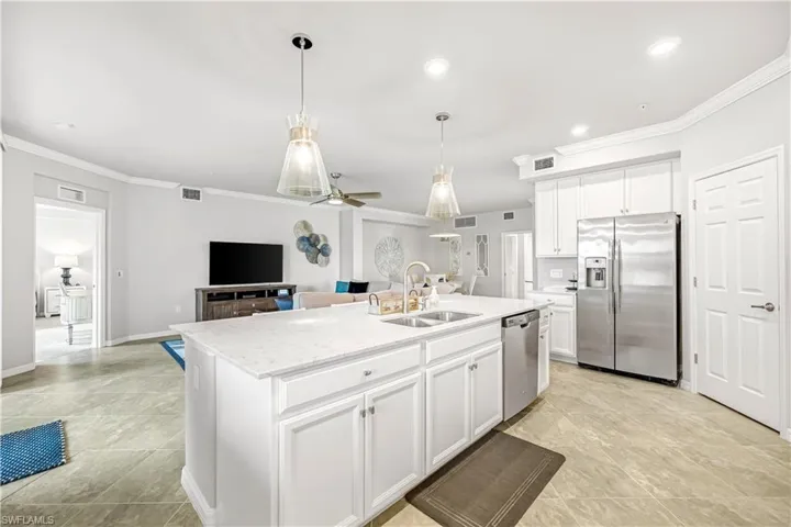 Kitchen featuring stainless steel appliances, hanging light fixtures, white cabinetry, ornamental molding, and open floor plan