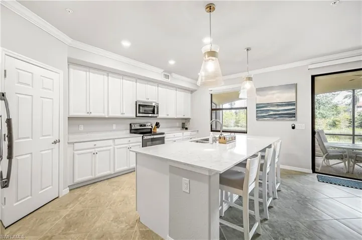 Kitchen with a kitchen breakfast bar, ornamental molding, an island with sink, appliances with stainless steel finishes, and white cabinets