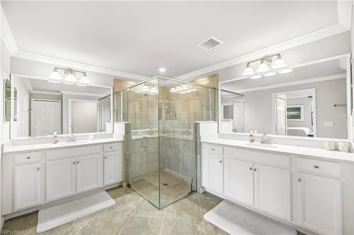 Ensuite bathroom with crown molding, a stall shower, two vanities, and light tile patterned floors