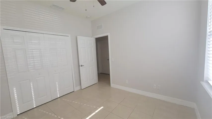 Guest bedroom featuring light tile patterned floors, ceiling fan, and a closet