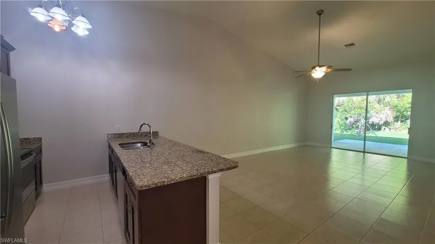 Kitchen featuring a ceiling fan, light tile patterned floors, light stone countertops, a chandelier, and open floor plan