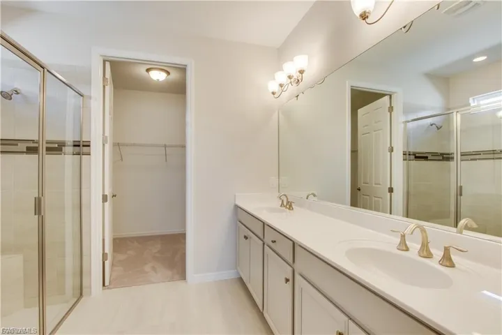 Full bath with a shower stall, double vanity, and a walk in closet