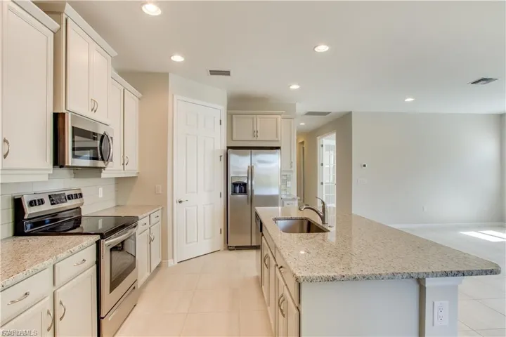 Kitchen featuring appliances with stainless steel finishes, light stone counters, an island with sink, light tile patterned floors, and recessed lighting