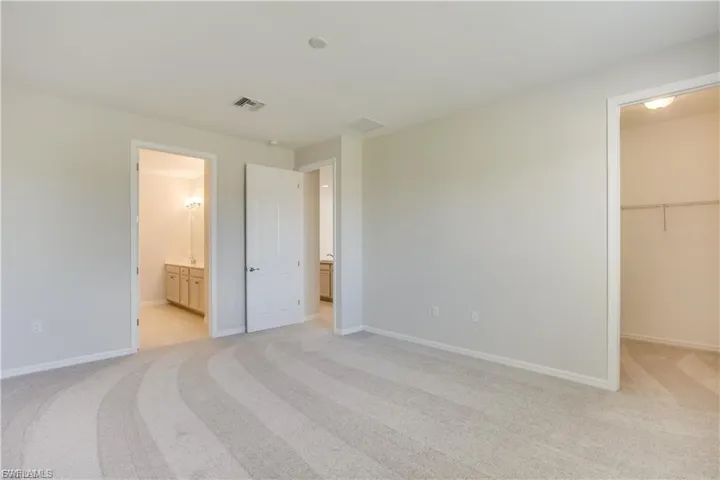 Unfurnished bedroom with a spacious closet, light carpet, and connected bathroom