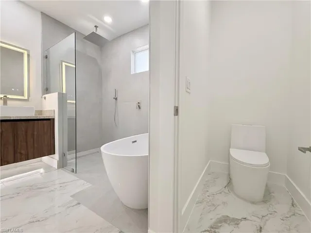 Master Bathroom featuring a shower stall, marble tiled flooring, vanity, a freestanding tub, and baseboards