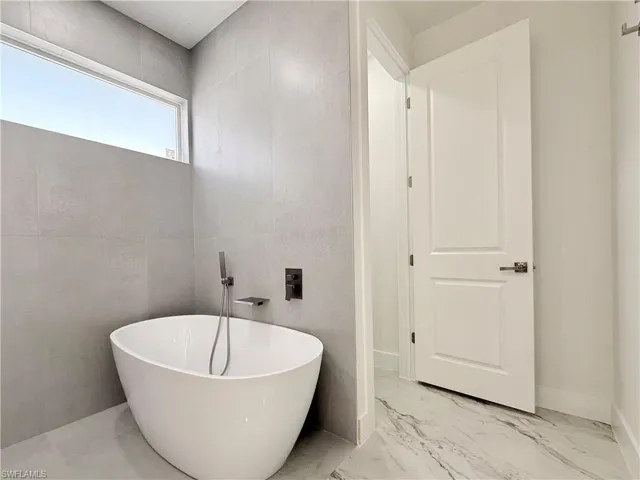 Master -Bathroom featuring a freestanding tub and marble finish flooring