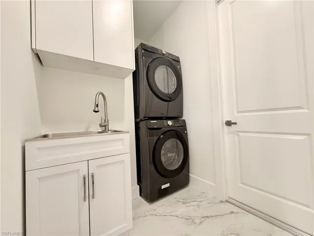 Laundry room featuring stacked washer / dryer, marble look tiles, cabinet space, and baseboards