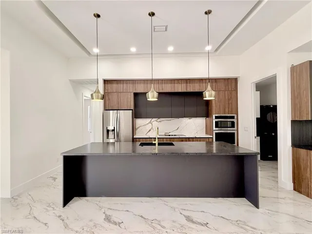 Kitchen with appliances with stainless steel finishes, modern cabinets, light marble finish flooring, pendant lighting, and a large island with sink