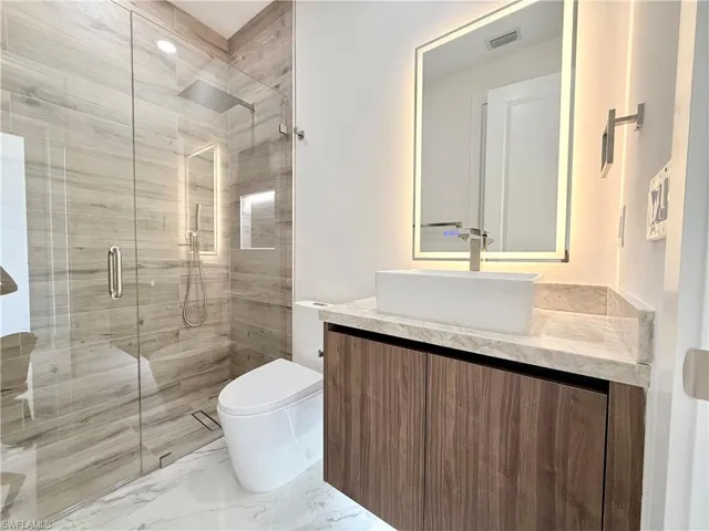 Bathroom with vanity, a shower stall, toilet, and marble finish floors