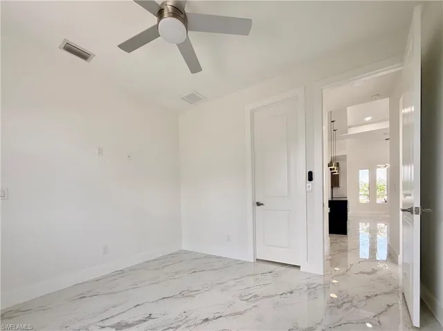 Empty room with ceiling fan, light marble finish floors, and baseboards